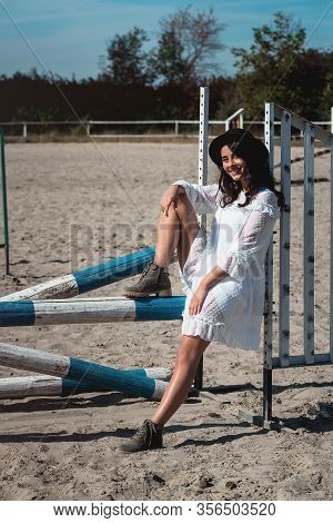 Beautiful Sexy Girl Posing On The Horizontal Crosspiece On A Horse Epodrom. Female Wearing White Dre