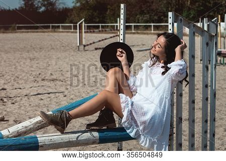 Beautiful Sexy Girl Posing On The Horizontal Crosspiece On A Horse Epodrom. Female Wearing White Dre