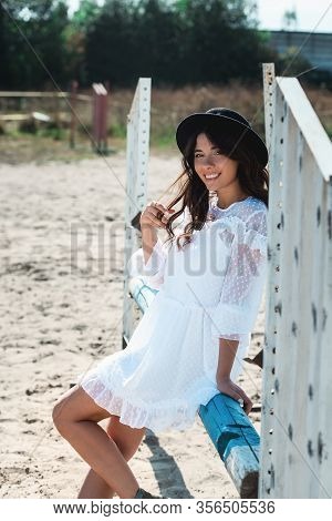 Beautiful Sexy Girl Posing On The Horizontal Crosspiece On A Horse Epodrom. Female Wearing White Dre