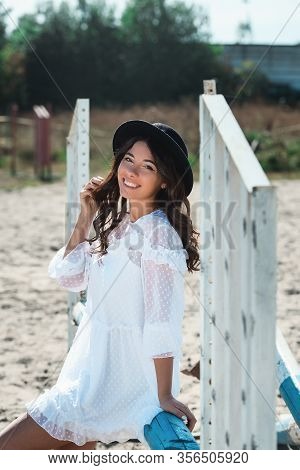 Beautiful Sexy Girl Posing On The Horizontal Crosspiece On A Horse Epodrom. Female Wearing White Dre