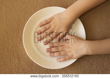 Childrens Little Hands Lie In An Empty White Plate On The Table