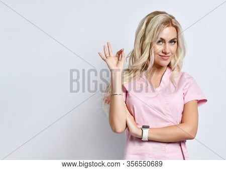 Blond Lady In A Pink Medical Suit, Smart Watch, Jewelry Posing Isolated On White. She Shows Her Fing