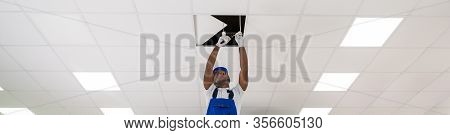 Young Male Electrician On Stepladder Installing Light On Ceiling