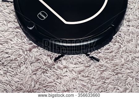Automatic Robot Vacuum Cleaner In Black On A Gray Shag Carpet. New Modern Technologies For Apartment