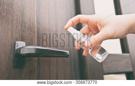 The wooman is applying sanitizer on the door handle