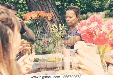 Friends Sitting At Table In Yard. Cropped Shot Of Cheerful Young Male And Female Friends Gathering A