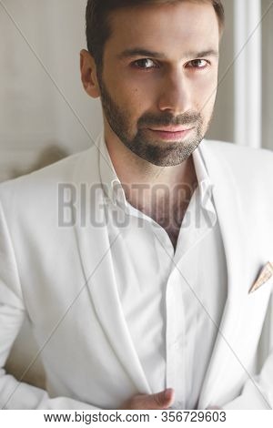 Elegant Young Handsome Man With A Beard In A White Classic Suit. The Hotels Interior. Photo Studio. 