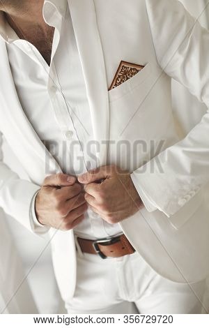 Elegant Young Handsome Man With A Beard In A White Classic Suit. The Hotels Interior. Photo Studio. 