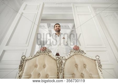 Elegant Young Handsome Man With A Beard In A White Classic Suit. The Hotels Interior. Photo Studio. 