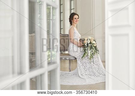 Beautiful Bride Posing In Wedding Dress In A White Photo Studio. Mirror. Sofa. Bouquet. The Door. Ch