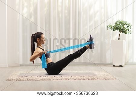 Young woman exercising with an elsatic band on the floor at home
