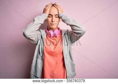 Beautiful sporty woman doing sport listening to music using headphones over pink background suffering from headache desperate and stressed because pain and migraine. Hands on head.