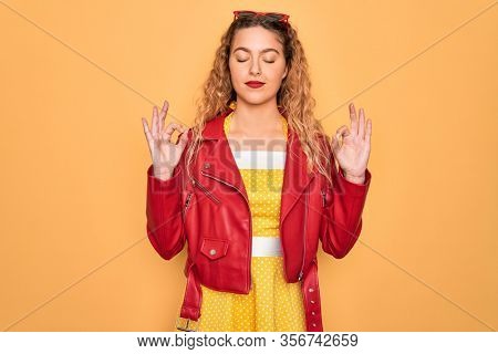 Young beautiful blonde woman pin-up with blue eyes wearing red sunglasses and jacket relax and smiling with eyes closed doing meditation gesture with fingers. Yoga concept.