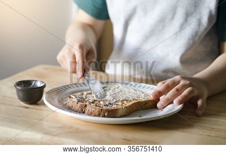 Cropped Image Of Kid Hands Spreading Butter On Bread, Child Applying Butter To Toast For His Breakfa
