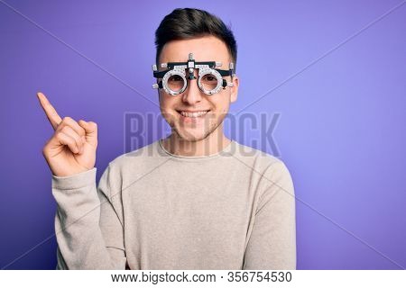 Young handsome caucasian man wearing optometrical glasses over purple background with a big smile on face, pointing with hand and finger to the side looking at the camera.