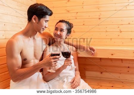 Asian Couples Toasting And Drinking Wine In Sauna Room For Celebrating Wedding Anniversary. Healthy 