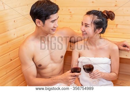 Asian Couples Toasting And Drinking Wine In Sauna Room For Celebrating Wedding Anniversary. Healthy 