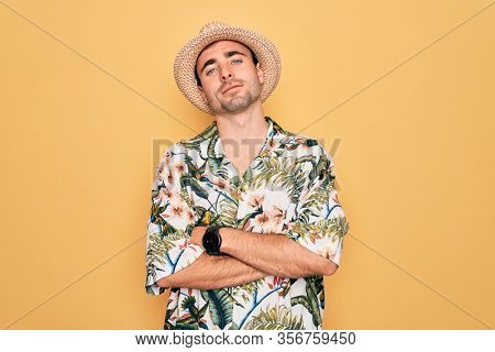 Young handsome man with blue eyes on vacation wearing summer florar shirt and hat happy face smiling with crossed arms looking at the camera. Positive person.