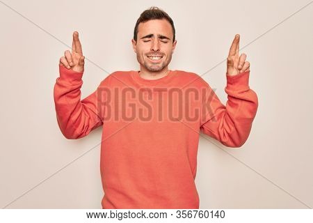 Young handsome man with blue eyes wearing casual sweater standing over white background gesturing finger crossed smiling with hope and eyes closed. Luck and superstitious concept.