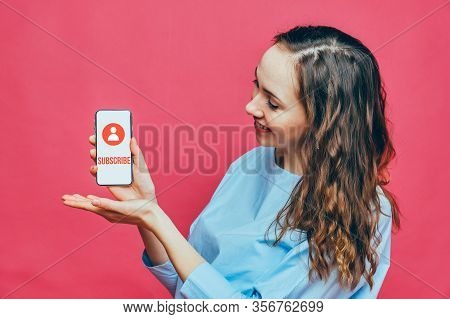 Stylish Caucasian Girl In A Pale Blue T-shirt On A Pink Background. The Concept Of Subscribing To A 