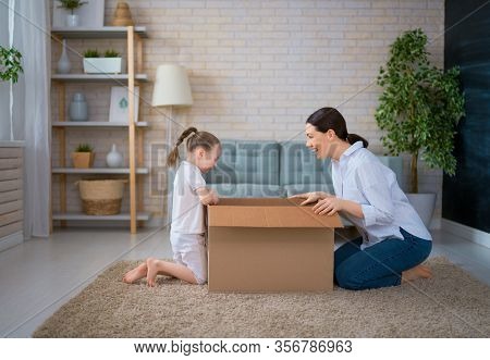 Mother and daughter are unpacking cardboard box at home. 