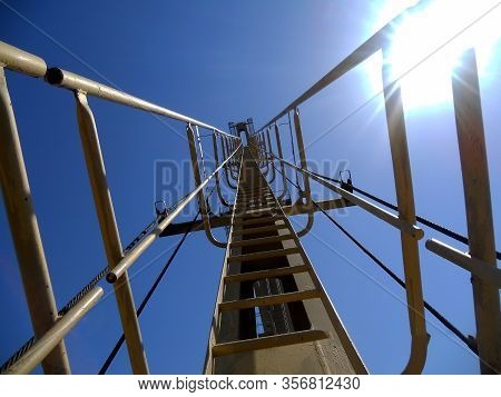 Construction Crane On A Background Of Blue Sunny Sky. Long Yellow Arrow Of A Construction Crane With
