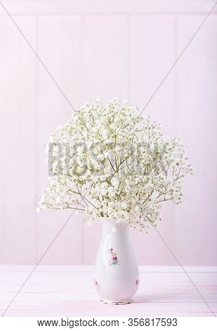 Small bouquet of Gypsophila flowers in porcelain vase against a light pink wooden background. Selective focus.