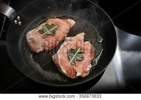 Chicken Saltimbocca Wrapped With Air-dried Ham And Sage Leaves Are Roasted In A Black Pan On The Sto