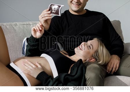 Couple Of Handsome Husband And Pretty Pragnant Woman Posing At Studio Embracing Stomach. Young Styli