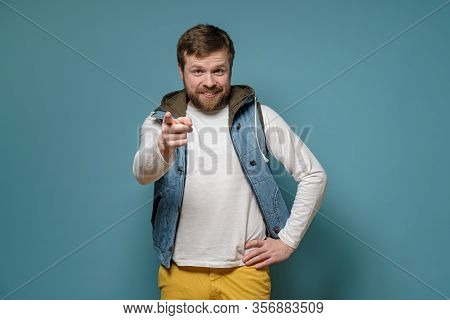 Cute Bearded Man Points At Someone With Index Finger And Blames, Smiles Slyly And Benevolent Looks, 