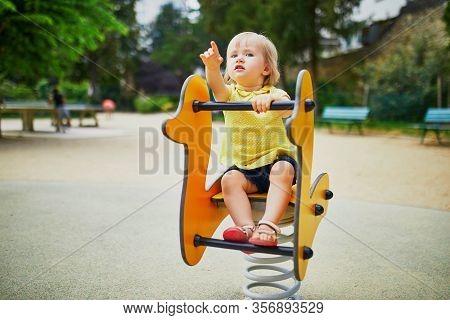 Adorable Toddler Girl Having Fun On Spring Rider On Playground. Outdoor Activities For Kids