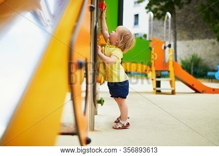 Adorable Toddler Girl On Playground Near Slide. Child Playing On The Street. Outdoor Activities For 