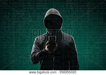 Dangerous Hacker With A Smartphone Gadget Over Digital Background With Binary Code. Obscured Dark Fa