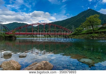 Red Bridge And River In The Mountain Valley. Japanese Countryside Landscape. Atera Valley In Kiso Va