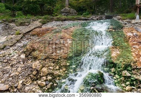 Hot Spring Running Through Rocks. Hot Spring Mineral Water Waterfall With Green Rocks