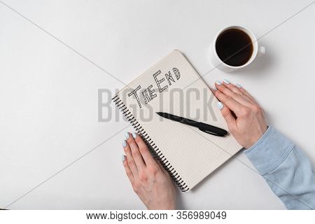 The End Notice On Notepad, Woman Hand, Notebook And Cup Of Coffee On White Background. Top View.