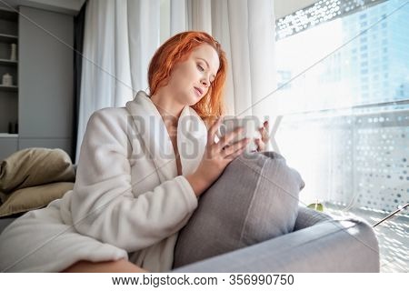 stayhome concept,  attractivewoman sitting in bed , holding cup of black coffee, enjoying peaceful calm weekend vacation morning time alone in bedroom at home or hotel.