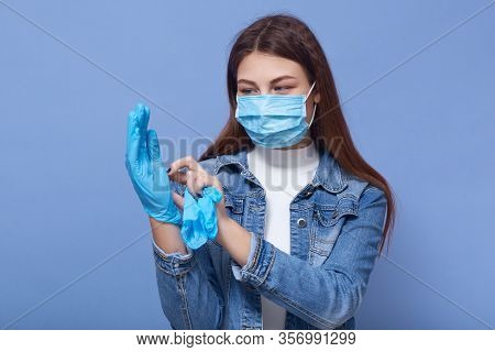 Horizontal Shot Of Female Wearing Denim Jacket And White Shirt, Adorable Girl Putting On Rubber Disp