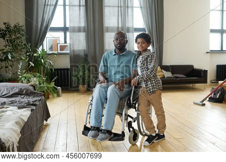 Portrait Of African Disabled Father Sitting In Wheelchair And Looking At Camera Together With His Li
