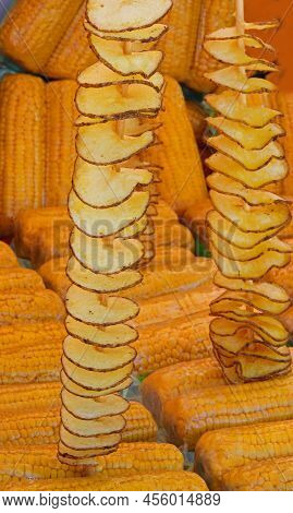Long Skewers Of Fried Potato Chips With Peel And Yellow Cooked Organic Corn Cobs With Plastic Wrap F
