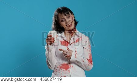 Creepy Looking Zombie With Deep Scars Smelling Coffee From A Cup On Blue Background. Frightening Cra