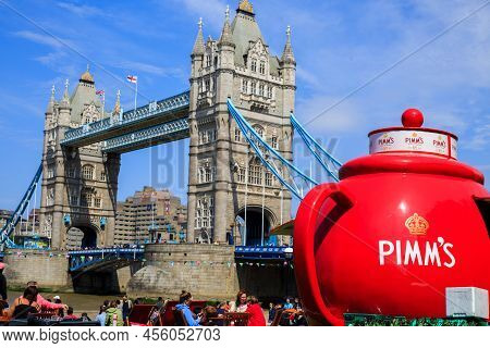 Tower Bridge, London, 2022.  A Bright Red Pimms Teapot Stands Next To The Tower On A Glorious Summer