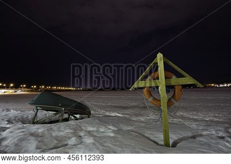 Rovaniemi, Finland - March 20th, 2022: A Night Scene Of Useless Life Boat And Life Wheel On The Bank