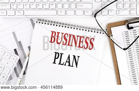 Text Business Plan On Office Desk Table With Keyboard, Notepad And Analysis Chart On A White Backgro