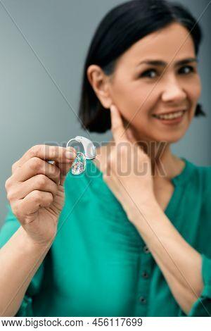 Treatment Of Deafness In Adult People. Woman Holding Bte Hearing Aid In Hand On Foreground And Point