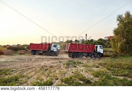 Two Red Dump Trucks Simultaneously Lifted The Bodies To Unload The Sand. Cargo Transportation Servic