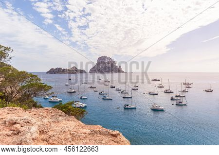 Anchored Catamarans And Sailing Yachts In Bay Cola D'hort Against Backdrop Of Two Lovely Rocky Islan