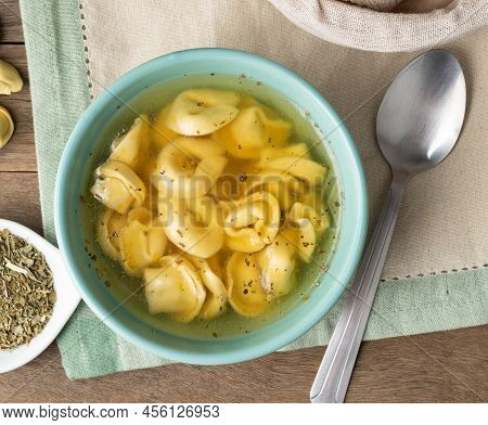 Cappelletti Or Tortellini Brodo Soup In A Bowl With Bread Slices And Seasoning Over Wooden Table.