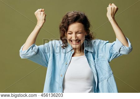Overjoyed Excited Happy Curly Pretty Lady In Jeans Casual Shirt Raise Hands Up With Joy Posing Isola
