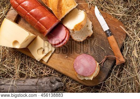 Cutting A Sandwich With A Knife With A Wooden Handle. Sausage, Cheese And Baguette On Cutting Board.